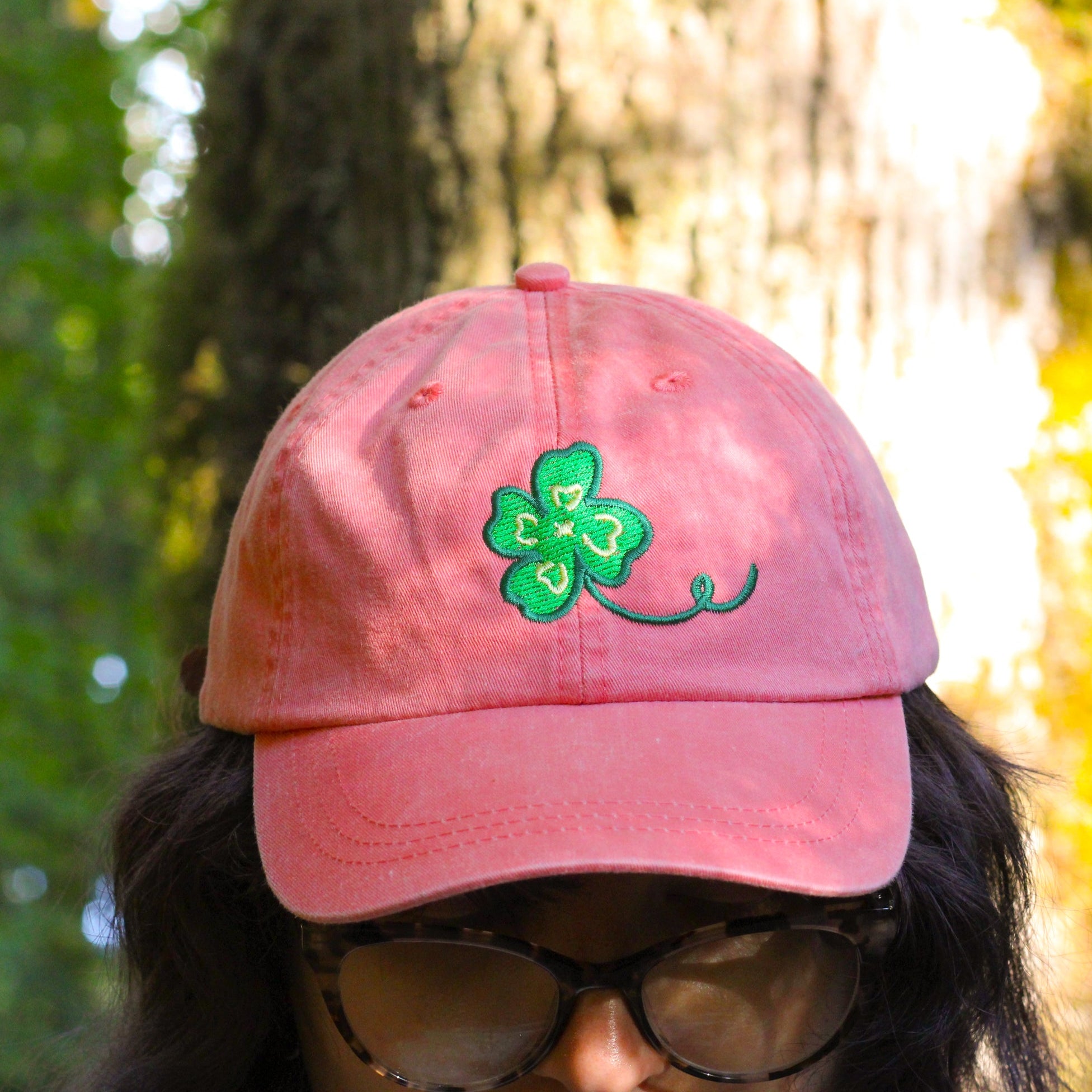Person wearing a pink cap with a green clover design in a forest setting