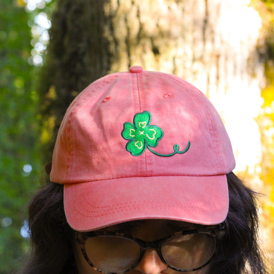 Person wearing a pink cap with a green clover design in a forest setting
